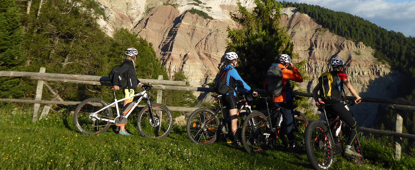 Quattro ciclisti su un sentiero panoramico tra la natura rigogliosa e le Dolomiti