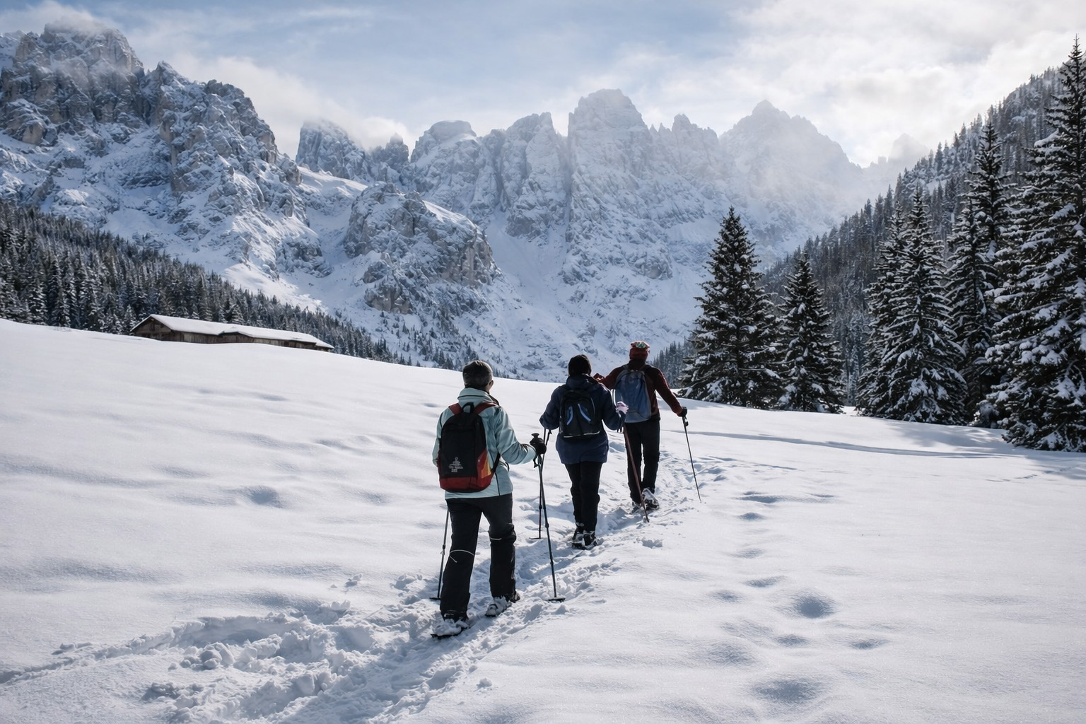 Tre escursionisti con zaini, bastoncini e ciaspole su un sentiero innevato