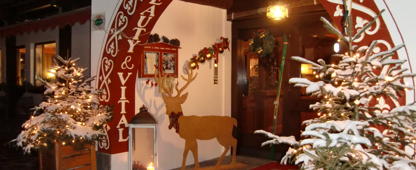 Ingresso principale con piante innevate illuminate, archi rossi e luci calde